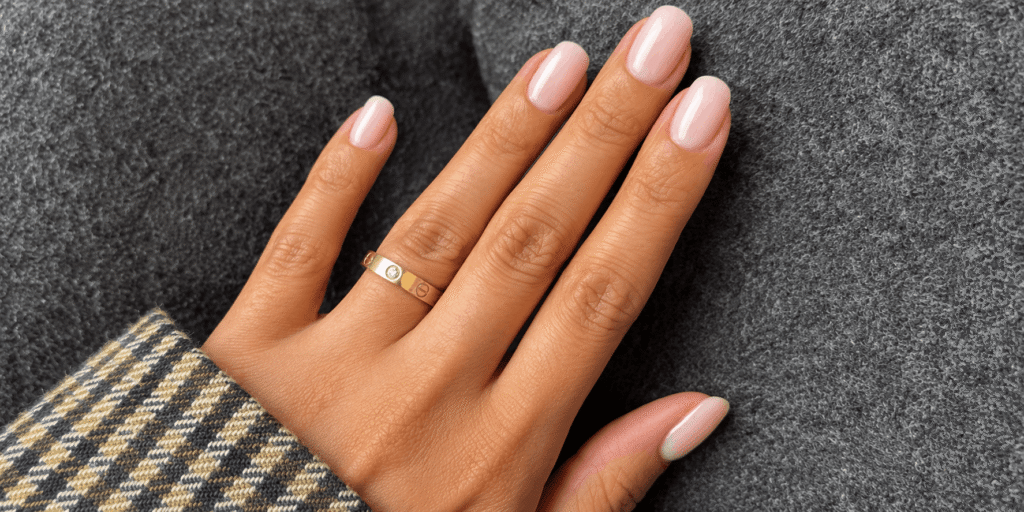 Glossy milky pink oval nails on a hand with a gold ring