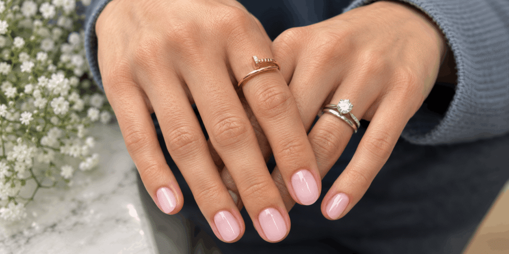Short glossy milky pink oval nails with elegant gold and diamond rings